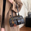 A brown trench coat features a black leather vintage letter print crossbody bag with gold hardware.