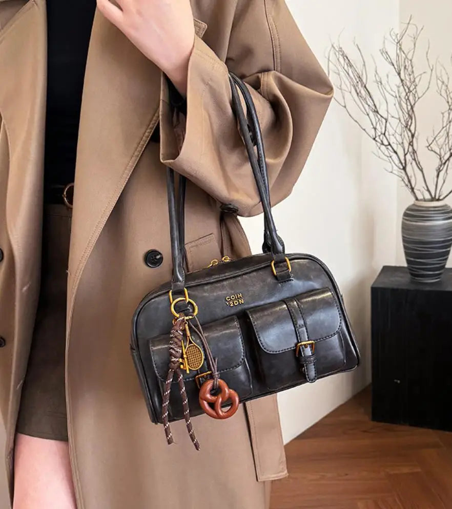 A brown trench coat features a black leather vintage letter print crossbody bag with gold hardware.