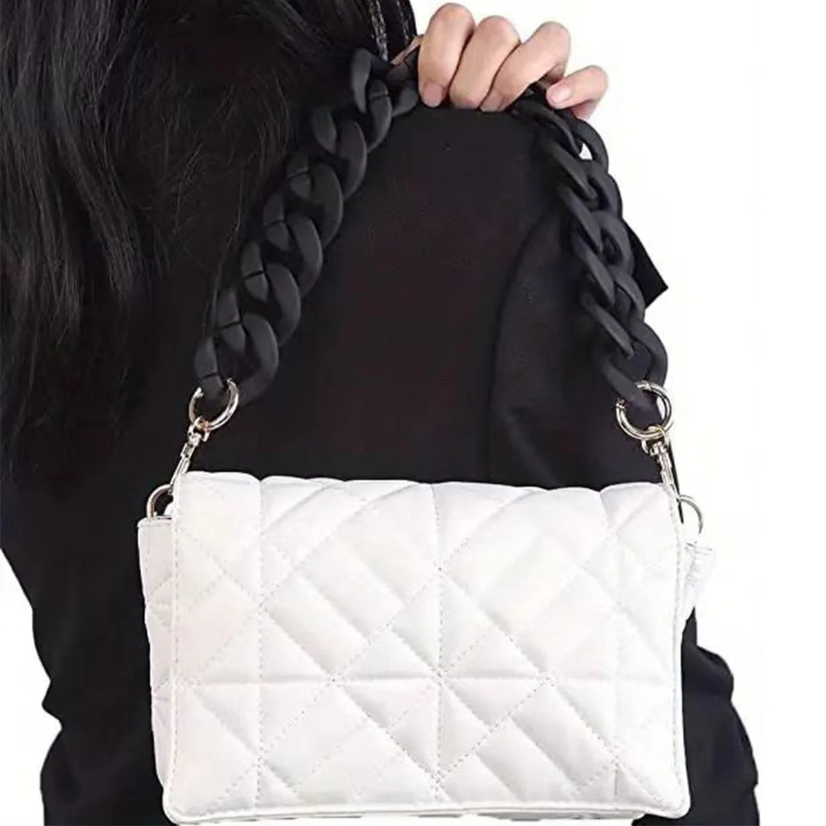 A white quilted flap handbag with a black chunky chain shoulder strap being held by a person.