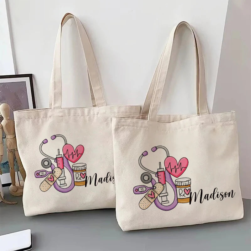A beige canvas tote bag featuring a pink stethoscope and heart design with the name Madison printed on it.