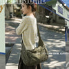 A woman wearing a cream knit sweater and dark skirt holds a large olive green cotton canvas shoulder crossbody bag.