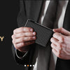 Hands holding a black magnetic card holder wallet against a dark suit jacket and patterned tie.