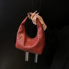 A close-up of a reddish-brown woven embossed hobo shoulder bag with a top handle being held by a hand.