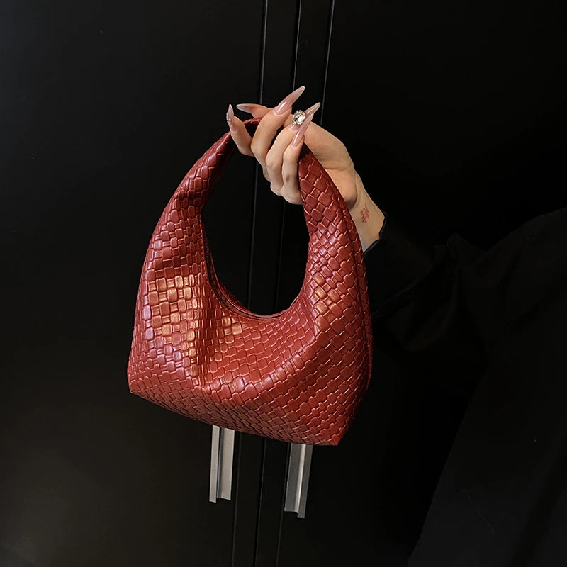 A close-up of a reddish-brown woven embossed hobo shoulder bag with a top handle being held by a hand.