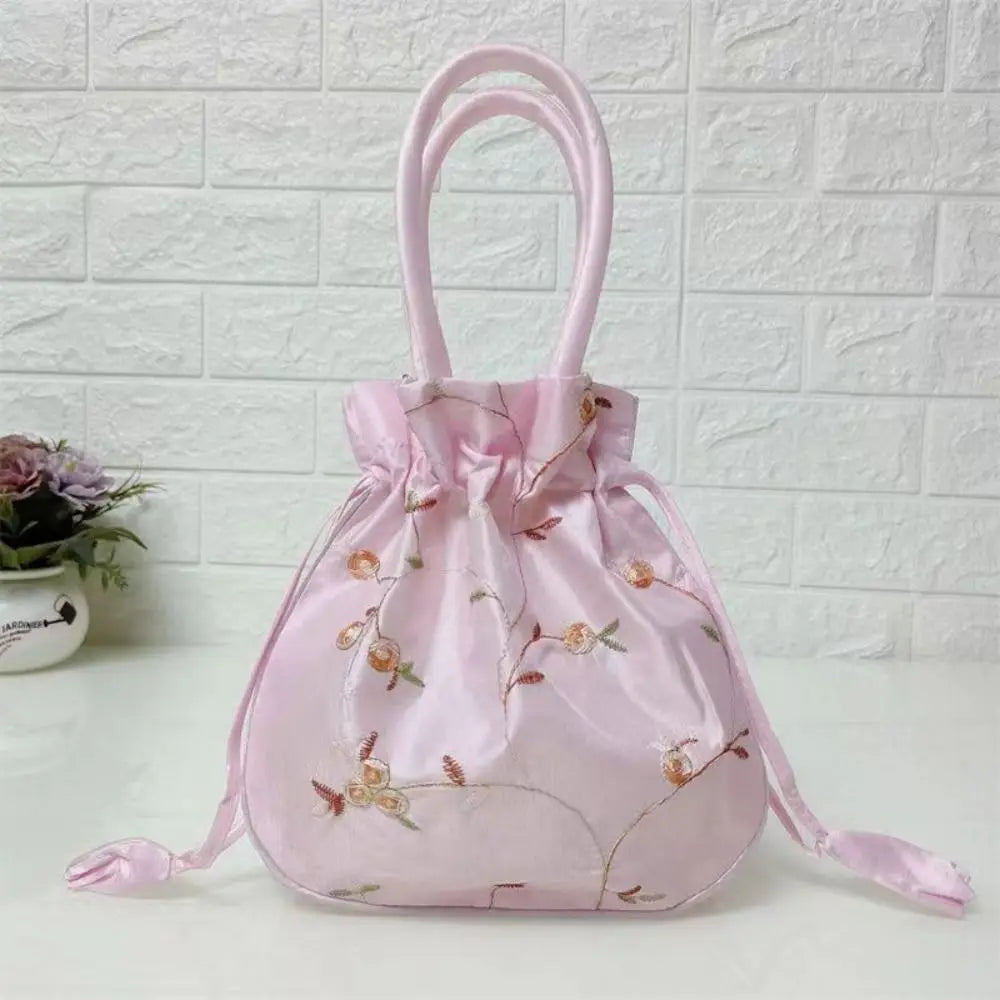 Clutch de noche rosa satinado con lazo bordado floral sobre una superficie blanca.