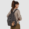 A woman wearing a beige long-sleeved shirt and brown pants carries a leopard print backpack.
