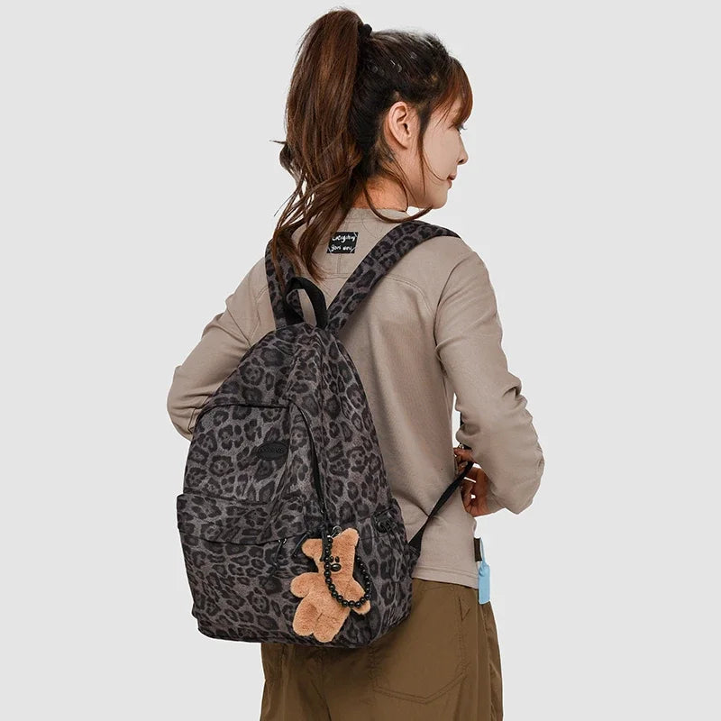 A woman wearing a beige long-sleeved shirt and brown pants carries a leopard print backpack.