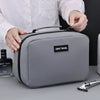 A person holds a gray portable waterproof travel toiletry bag with a black strap and a black label on it.