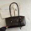 A dark brown leather tote bag with gold hardware resting on a white textured surface.