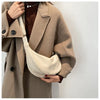 A woman wearing a beige wool coat is holding a cream-colored preppy sling crossbody bag.