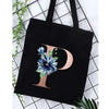 Black canvas tote bag featuring a large gold letter P with blue floral accents