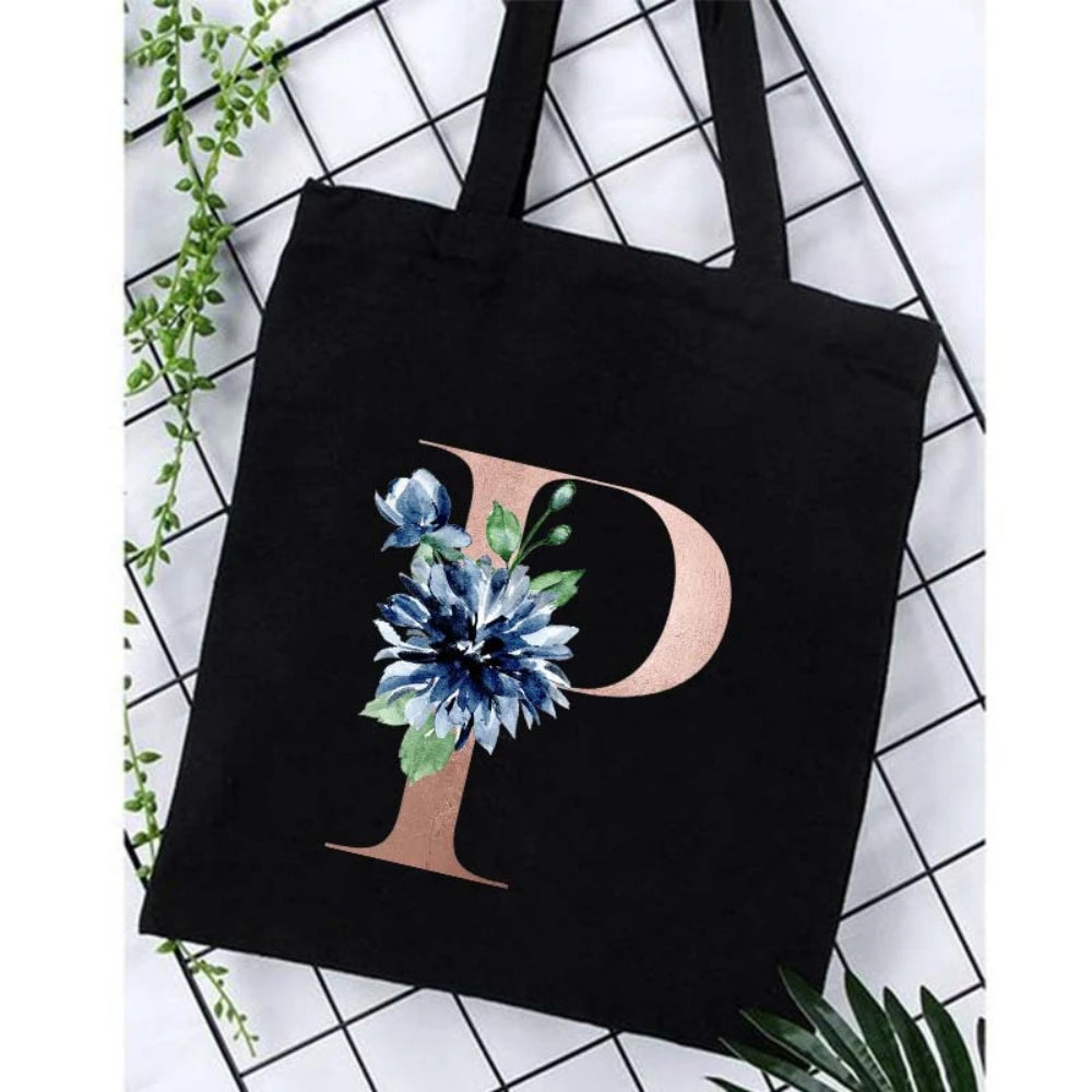 Black canvas tote bag featuring a large gold letter P with blue floral accents