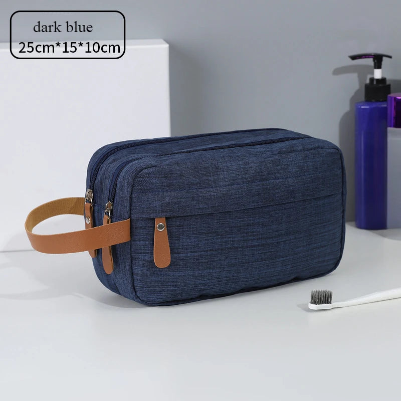 A dark blue portable travel storage pouch with a tan strap is shown on a white surface next to a toothbrush and a purple bott
