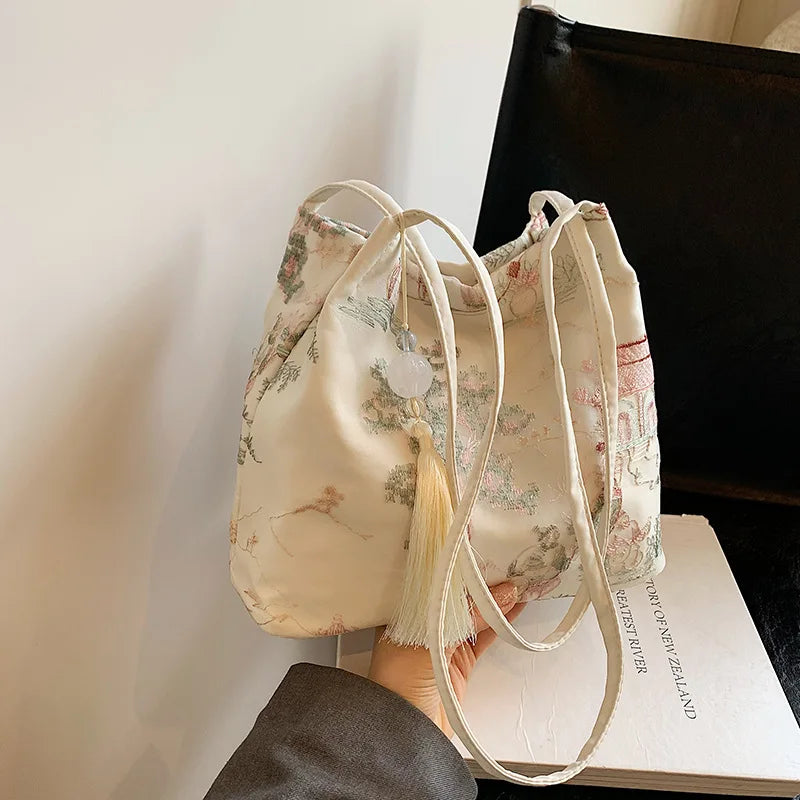 Bolso de seda jacquard color crema con bordado floral y cordones blancos largos sobre un libro.