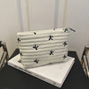 A white quilted makeup pouch with black embroidered flowers and a zipper, displayed on a black surface.