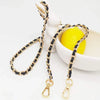 Gold and black braided metal shoulder strap for a crossbody bag displayed next to a yellow lemon