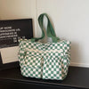 A green and white checkered corduroy tote bag with fabric handles resting on a dark surface.