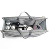 A gray handbag with an interior organizer insert showing various small cosmetic and jewelry items.