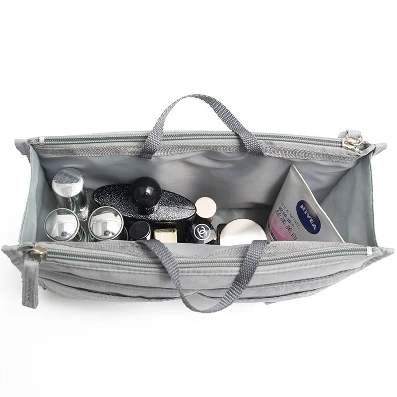 A gray handbag with an interior organizer insert showing various small cosmetic and jewelry items.