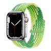 A silver Apple Watch is shown resting on a green braided stretch band.