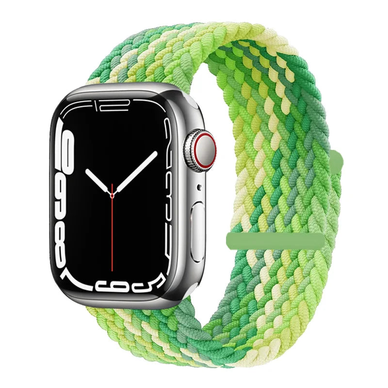 A silver Apple Watch is shown resting on a green braided stretch band.