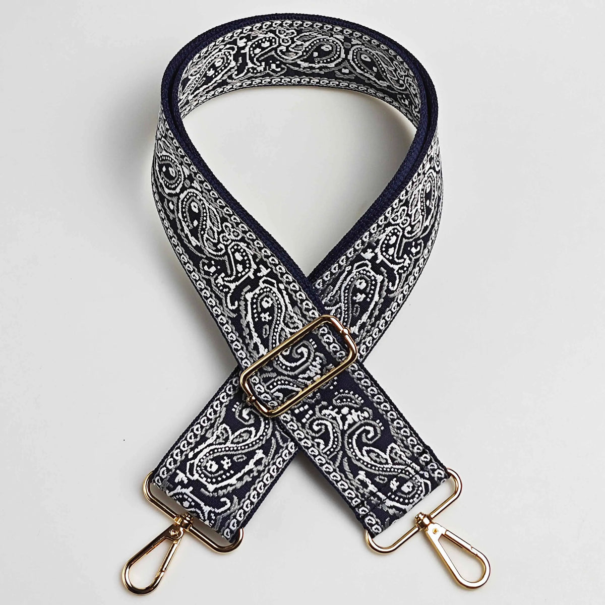 Correa ajustable cruzada de color azul marino oscuro y blanco con estampado paisley y herrajes dorados.
