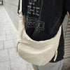 A beige soft nylon crossbody shoulder bag worn by a person, featuring black text on the shirt.