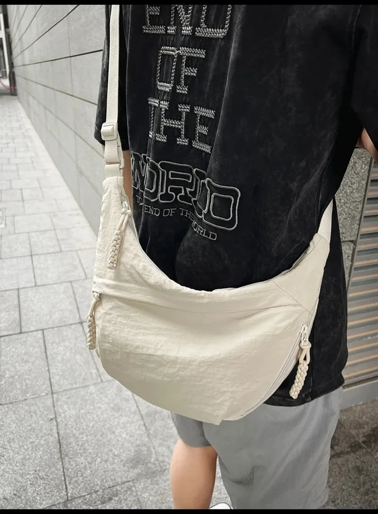 A beige soft nylon crossbody shoulder bag worn by a person, featuring black text on the shirt.