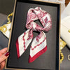 Elegant paisley silk hair scarf tied in a knot with red trim displayed in a black box.
