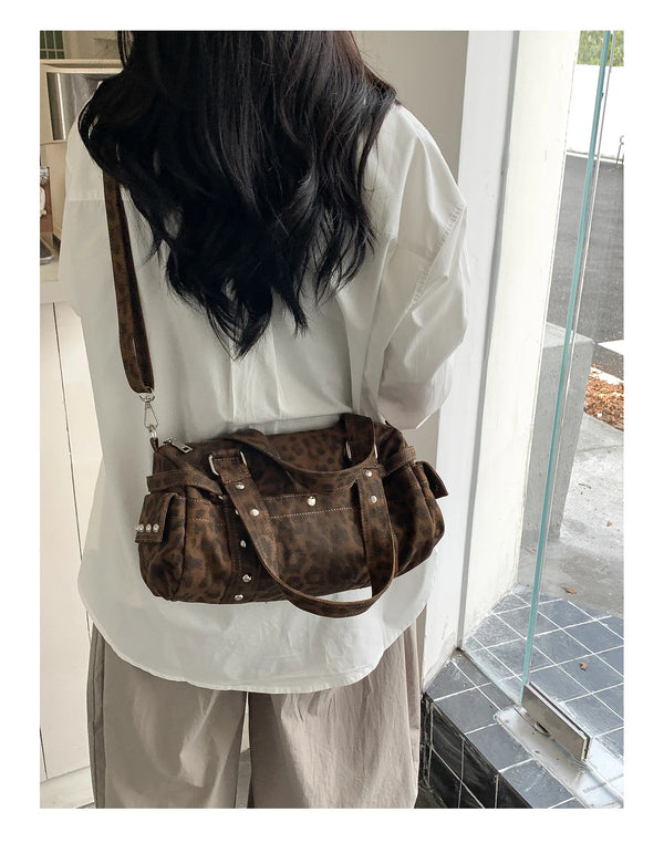 A woman is holding a brown leopard print Rivet Boston shoulder bag against a white shirt.