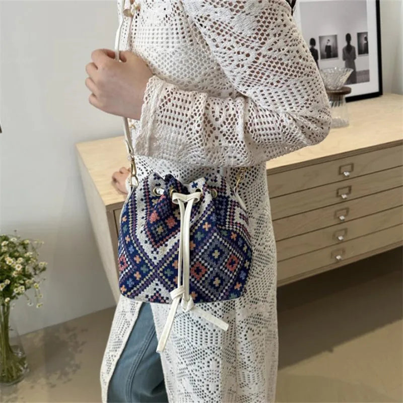 A woman is holding a floral drawstring bucket bag in blue and white patterns against a light background.