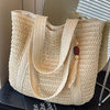 A natural straw woven tote bag with light beige color displayed on a surface.