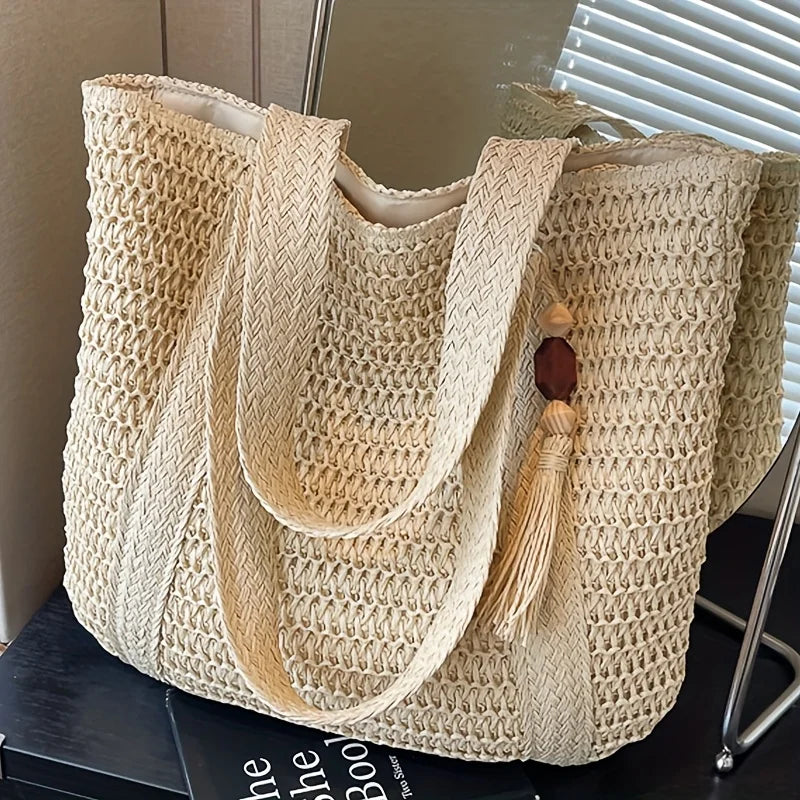 A natural straw woven tote bag with light beige color displayed on a surface.