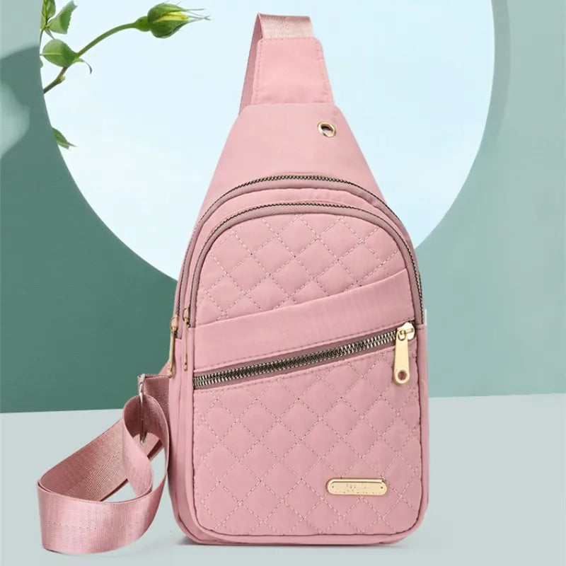 Pinkes gestepptes wasserdichtes Crossbody-Sling-Bag mit Reißverschluss und Trageriem auf grünem Hintergrund.