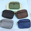 A collection of five nylon mini coin purses and card holders in shades of olive green, black, brown, gray, and blue arranged 