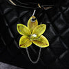 A yellow and green orchid flower keychain hanging from a black leather jacket.