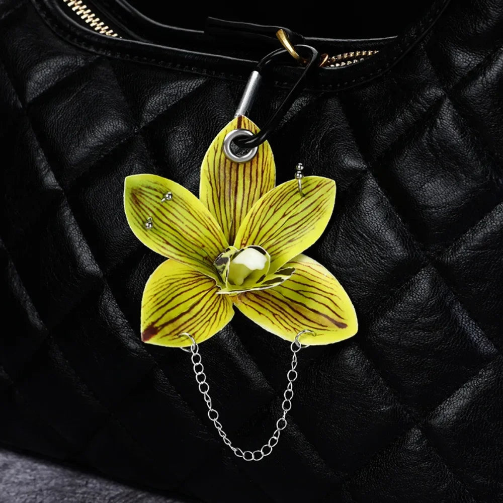 A yellow and green orchid flower keychain hanging from a black leather jacket.