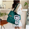 A woman holds a dark green canvas tote bag featuring a white Snoopy design in a casual indoor setting.