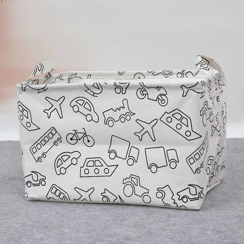 A white foldable fabric storage basket with handles featuring line drawings of various vehicles and objects.
