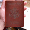 A brown leather passport holder with embossed text and an eagle emblem is held in a hand.