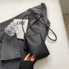 Bolso cruz de cuero negro sobre un blazer gris y un accesorio transparente.