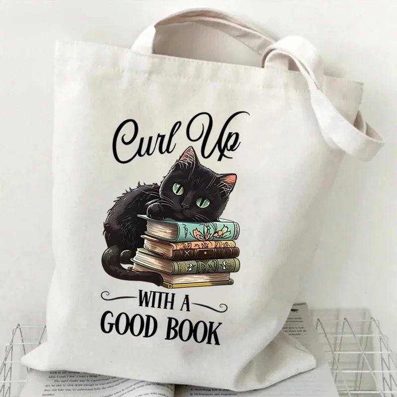 A white canvas tote bag featuring a black cat sitting on a stack of books with the text With a good book.