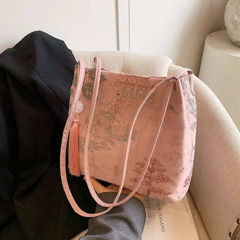 Un bolso de hombro de seda jacquard rosa retro junto a un abrigo negro en un sofá de color claro.