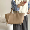 Un sac à main en cuir PU beige clair de style décontracté porté par une personne vêtue d'un pull blanc et d'une chemise à car