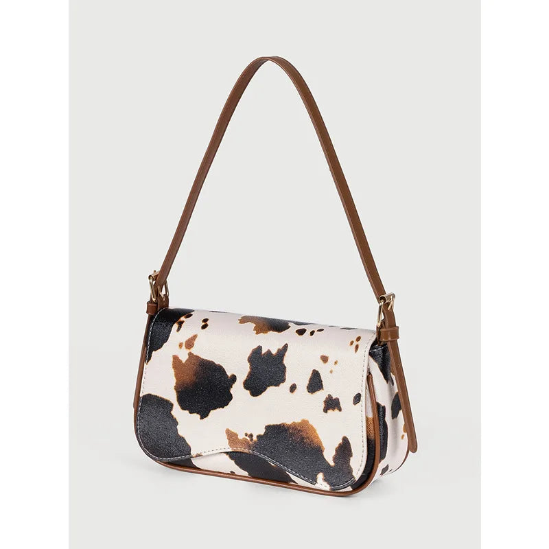 A beige and black cow print single shoulder bag with a brown adjustable strap.