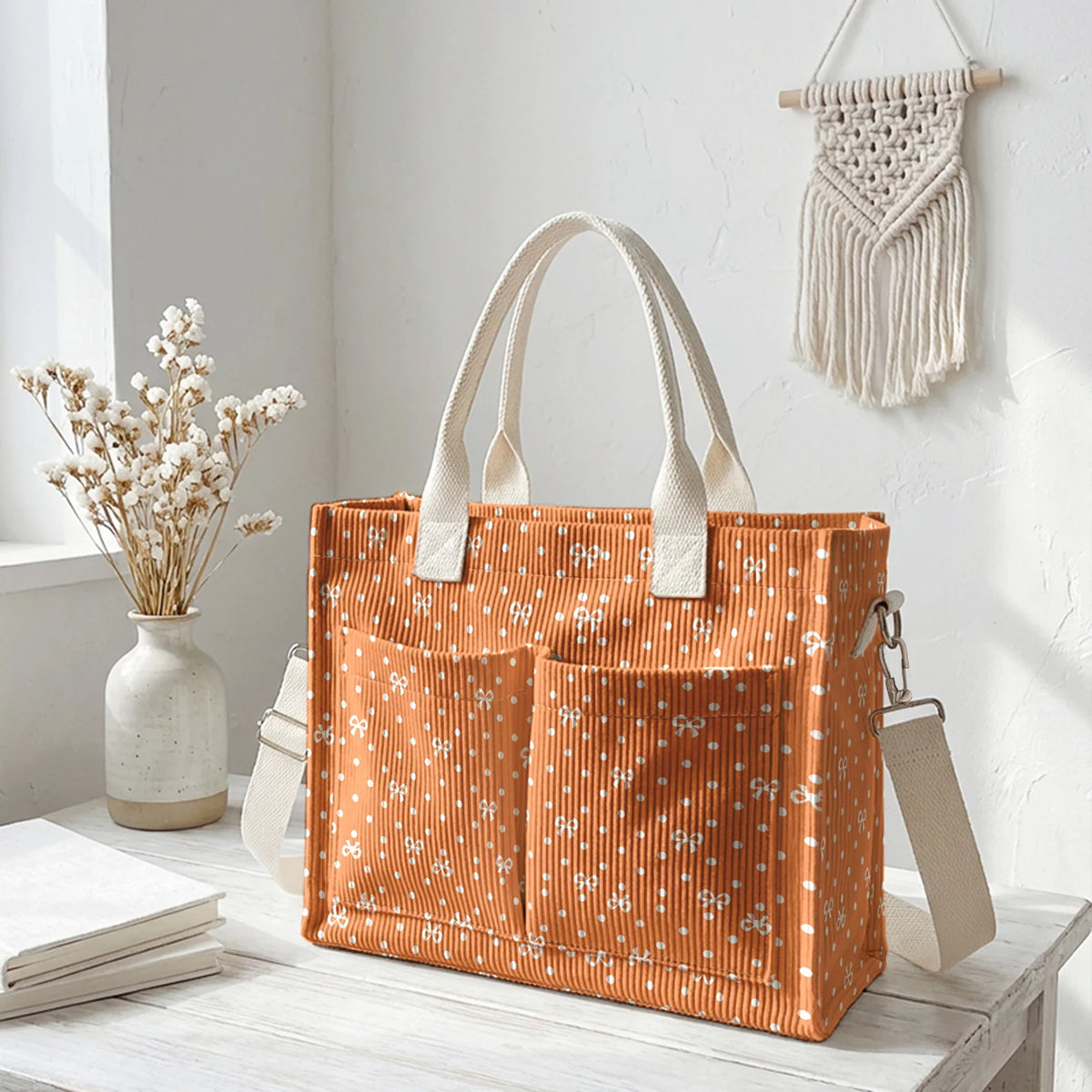 Sac en corduroy orange à pois blancs accroché au mur à côté de fleurs séchées.