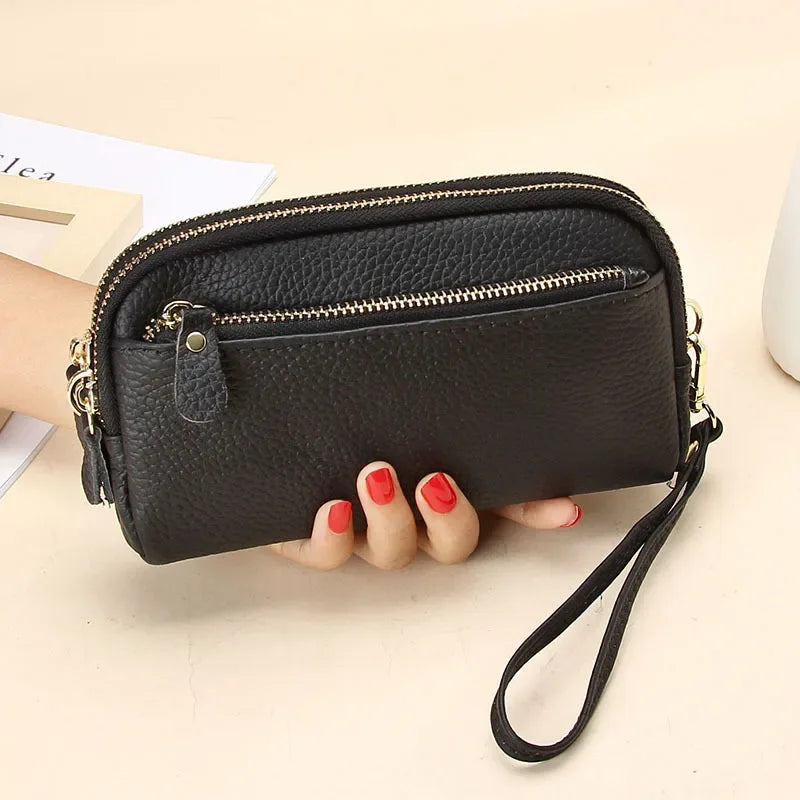 A black genuine cowhide leather double-zip wristlet wallet is shown being held by a hand on a light surface.