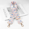 A pink and blue floral patterned diagonal shoulder strap is displayed next to its packaging box.