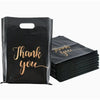 A black plastic gift bag with gold script text that reads Thank you, shown next to a stack of similar bags.