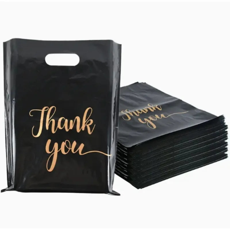 A black plastic gift bag with gold script text that reads Thank you, shown next to a stack of similar bags.